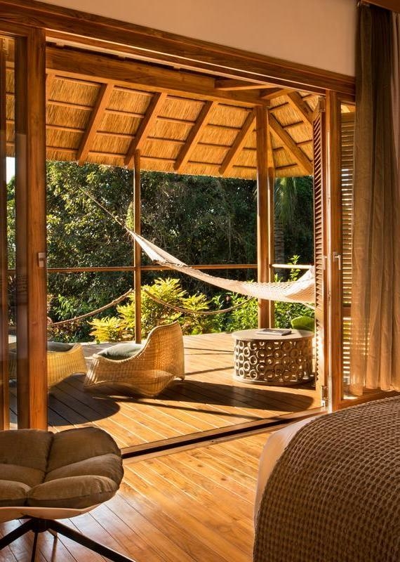 View from a bedroom onto a wooden deck with a hammock and lounge chairs surrounded by tropical trees at Zuri Zanzibar.