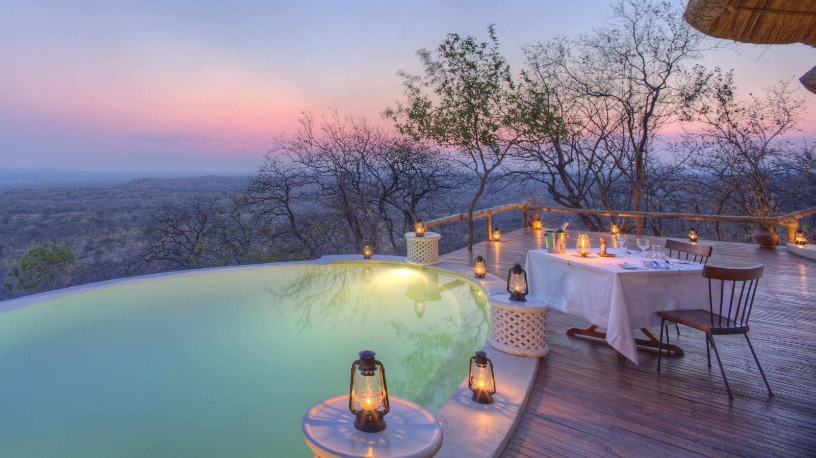 Private dining at Ikuka Safari Camp, featuring an intimate table set up for two next to a swimming pool surrounded by lanterns.