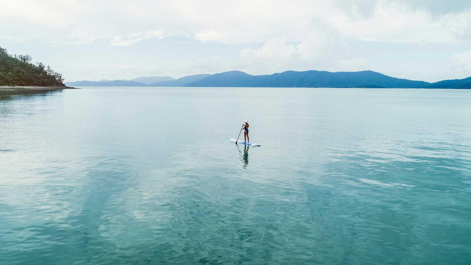 A woman standing on a paddle board paddling through still water