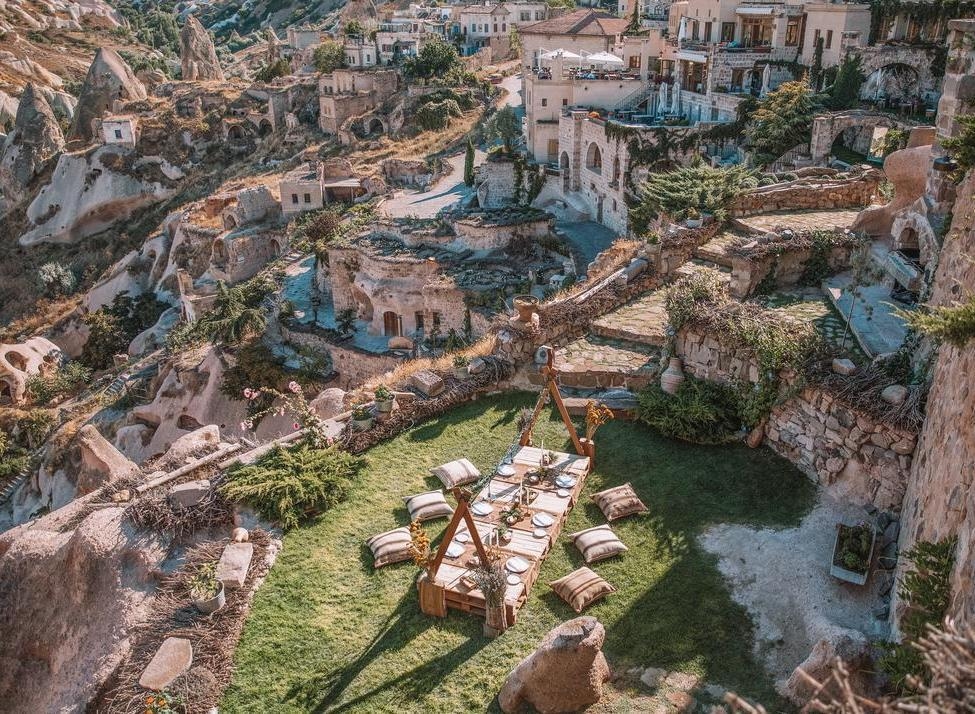 Low dining table with pillows on a green terrace overlooking the stone cave architecture of Argos in Cappadocia.