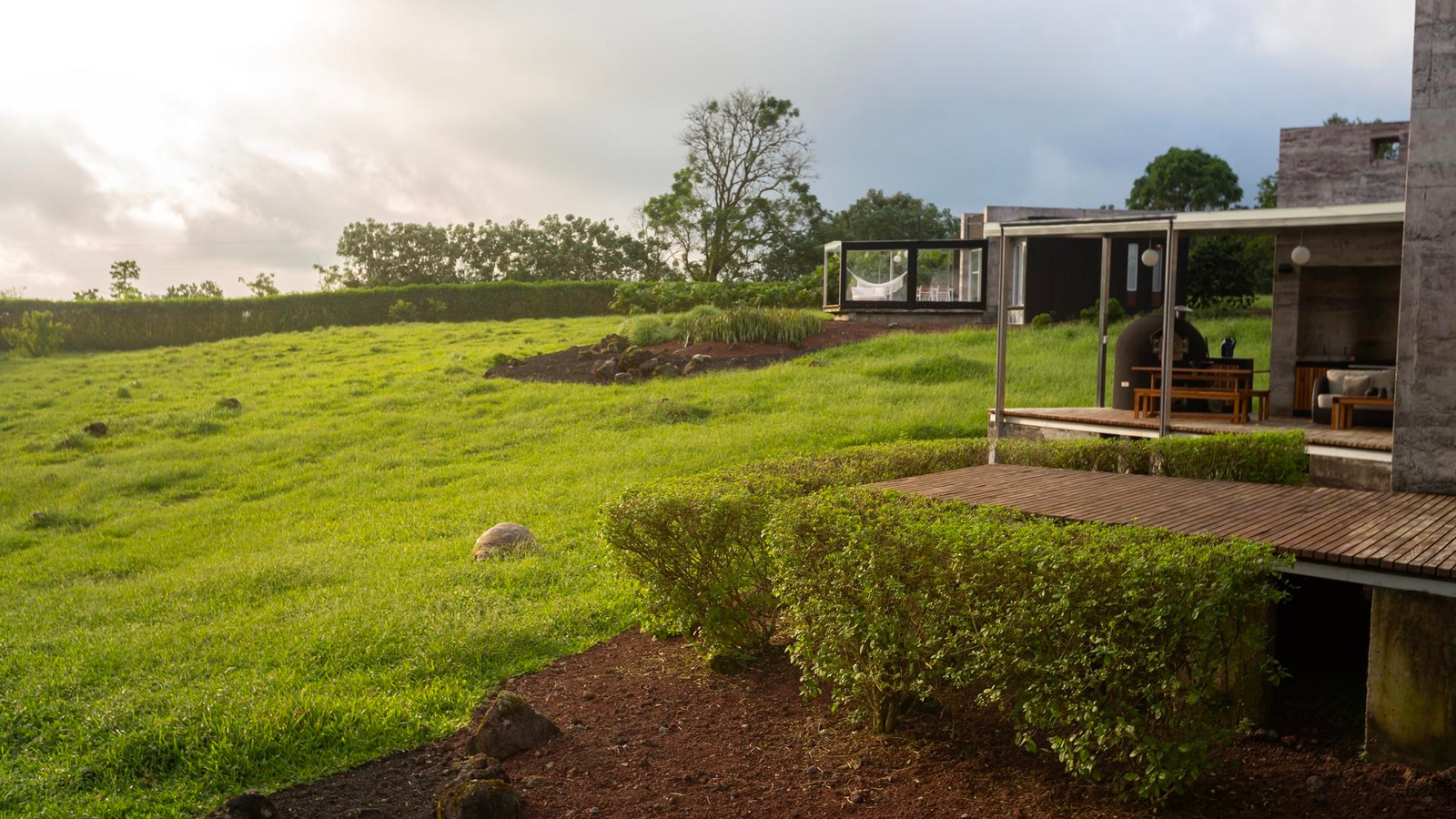 Modern house with large windows beside a lush green field under a cloudy sky.