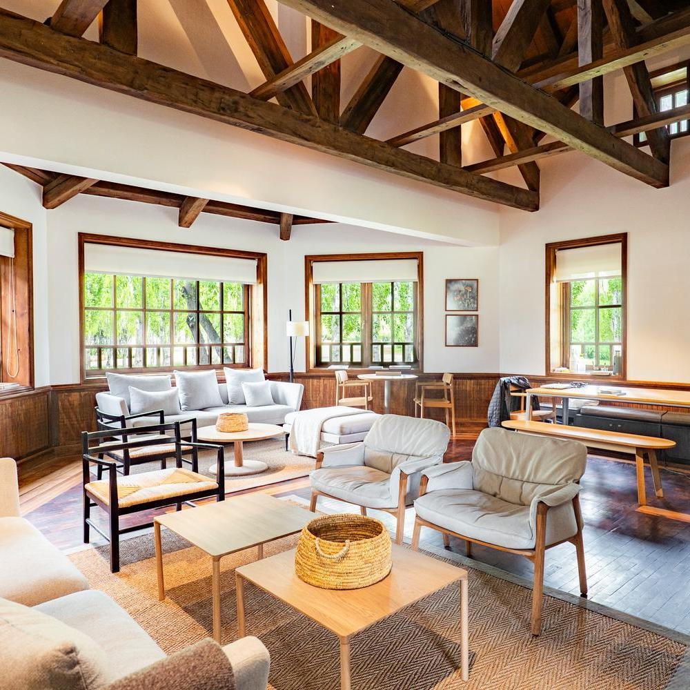 A cozy sitting room with armchairs, wooden coffee tables, and large windows at Explora Patagonia National Park.