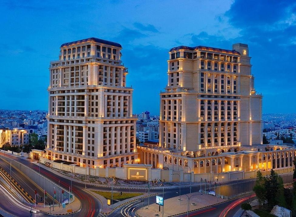 Two grand, lit-up luxury hotel towers at night overlooking the city streets and skyline of Amman, Jordan.