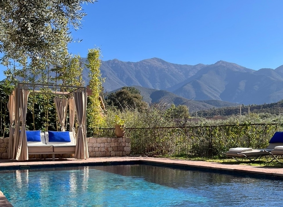 A luxury swimming pool with blue cushioned loungers and a cabana overlooking the Atlas Mountains in Morocco.