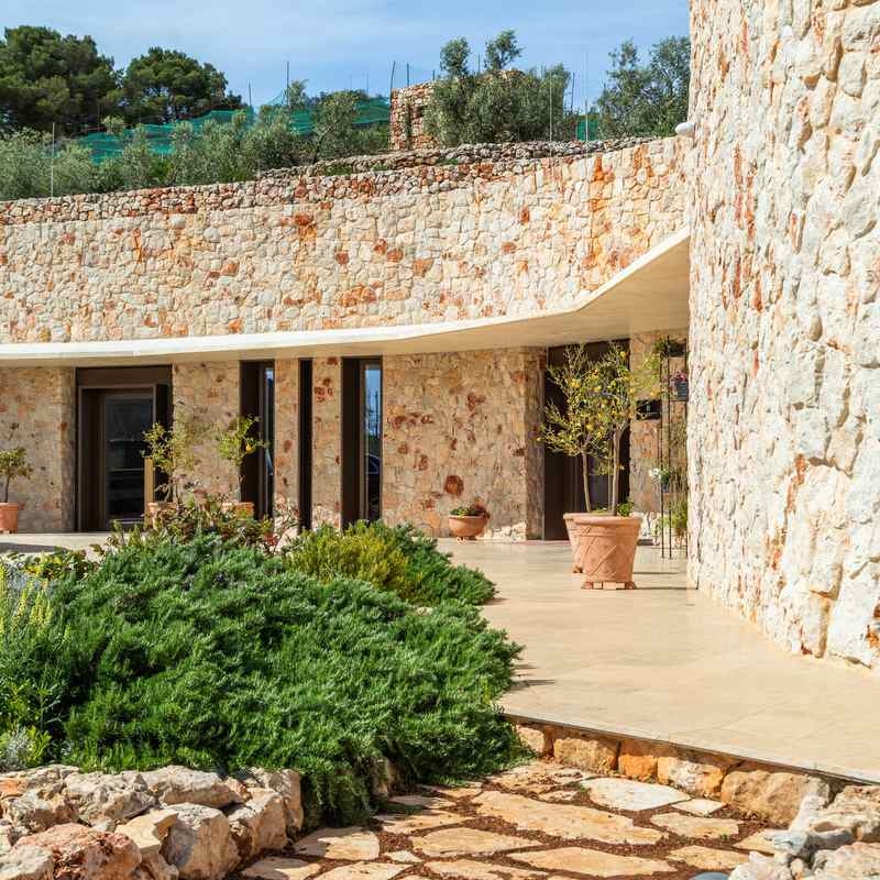 The exterior of Villa Nai 3.3 featuring a long, curved wall made of light-colored natural stone.
