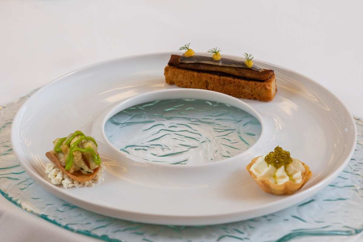 An artistic culinary dish displaying three small, meticulously prepared gourmet appetizers on a white plate.