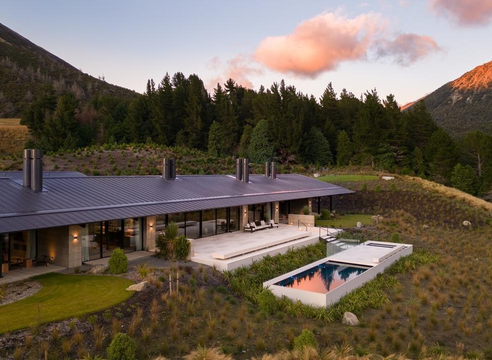 Aerial view of the Homestead at Flockhill Lodge, with a swimming pool, patio, and forest surrounded by mountains at sunset.
