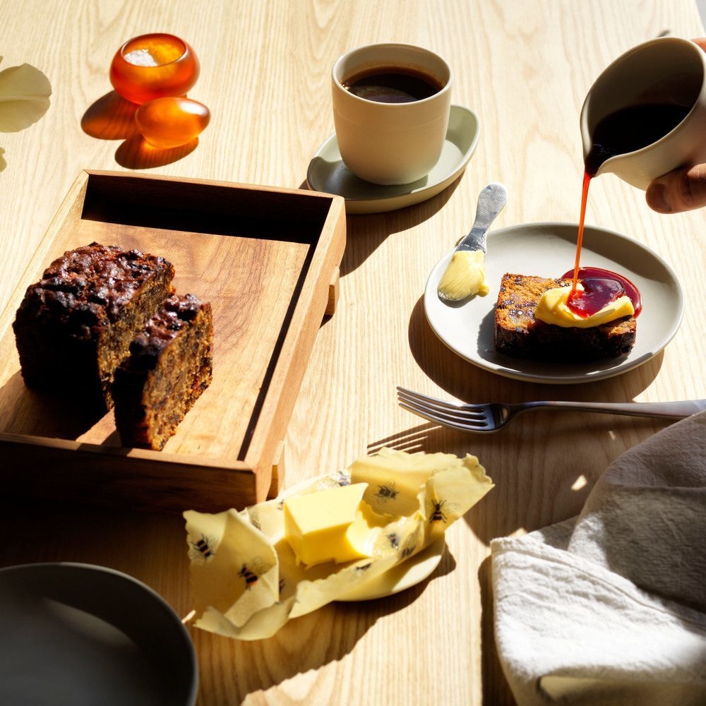 Sliced loaf cake on a tray with butter, coffee, and sauce pouring onto a slice.