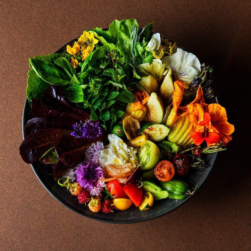 Top-down view of a salad bowl arranged with fresh greens, edible flowers, tomatoes, and berries.