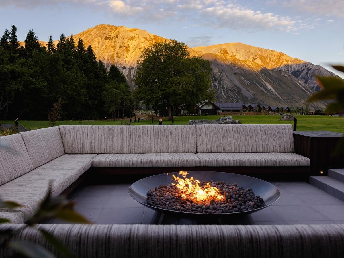 Outdoor lounge area with a burning fire pit, large sectional seating, and mountains in the background.