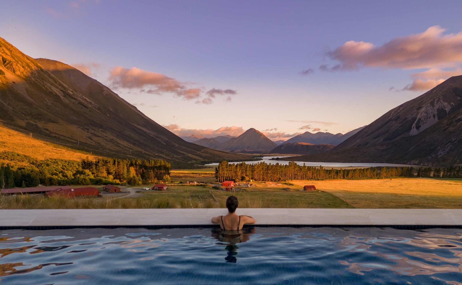 View from behind a person in an infinity pool looking out at a mountain valley landscape at dawn.