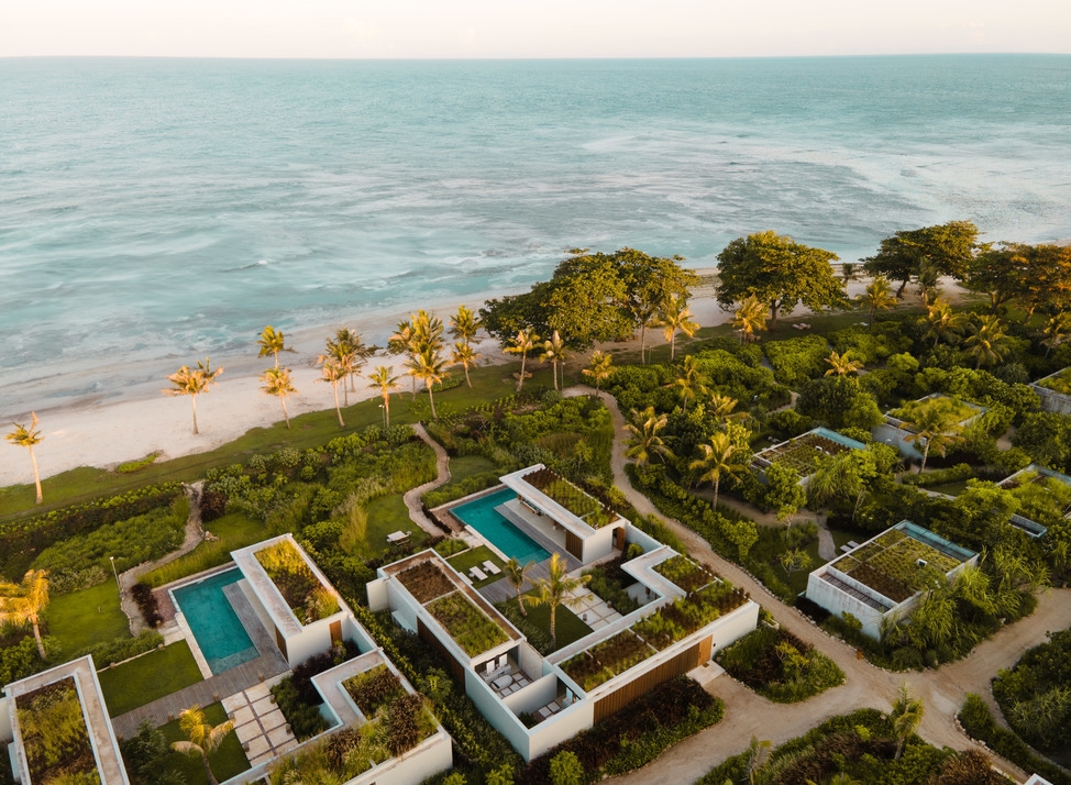 Aerial view of Cap Karoso's modern beachfront villas with green roofs and turquoise pools along a tropical coastline.