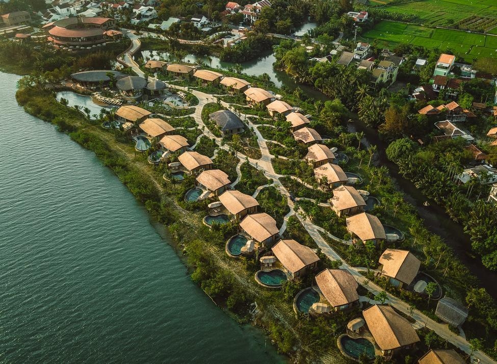 : Aerial landscape of Namia River Retreat's luxury villas situated between a wide river and green tropical foliage.