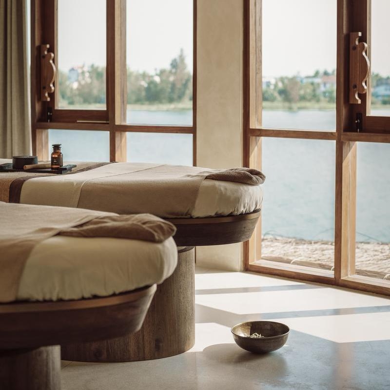 A luxury spa treatment room with massage tables and large windows overlooking the water.