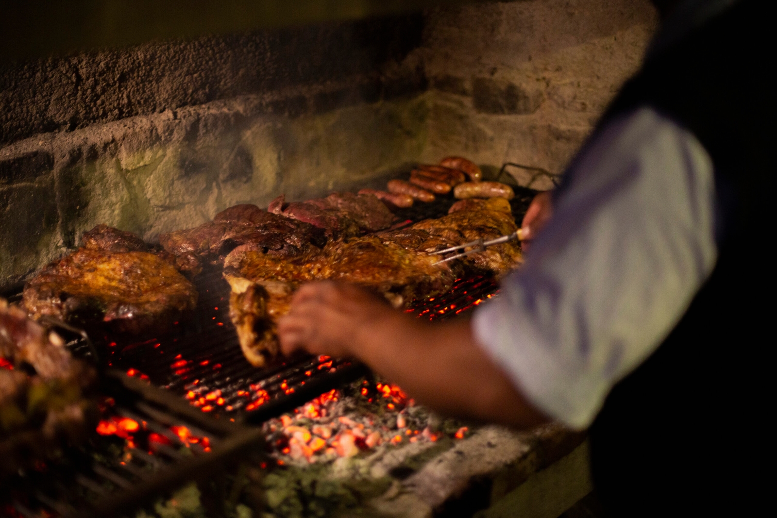 Person grilling various meats over a charcoal barbecue.