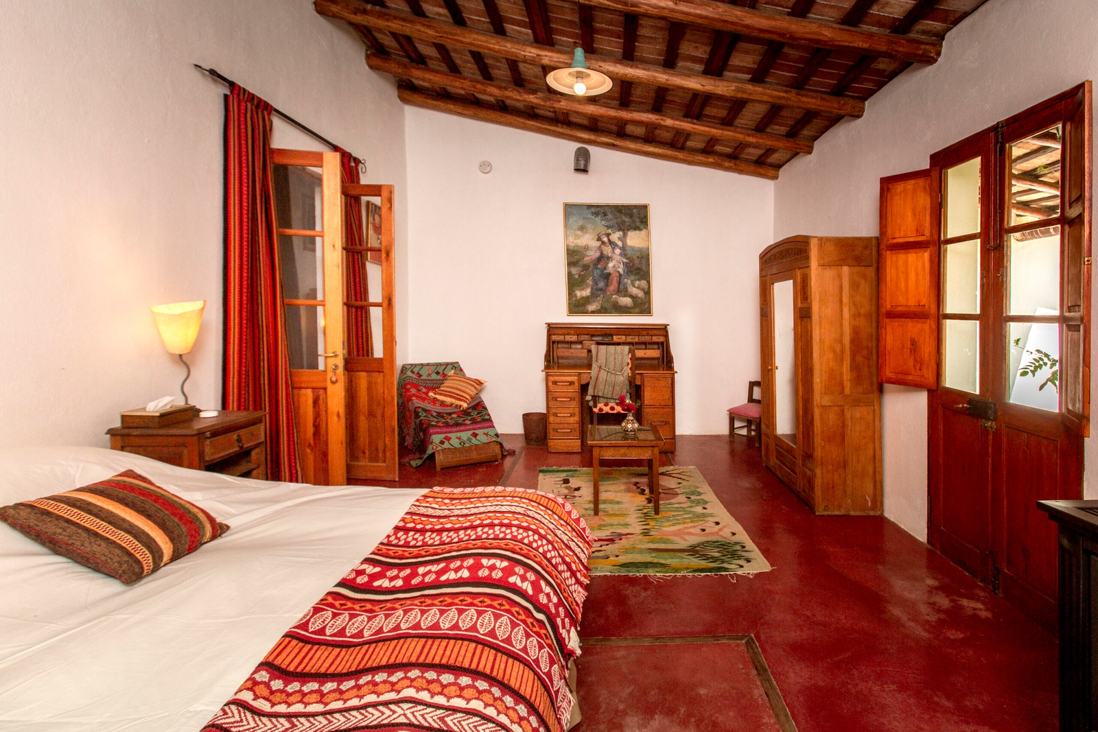 Rustic bedroom with a patterned bedspread, wooden furniture, and beamed ceiling.