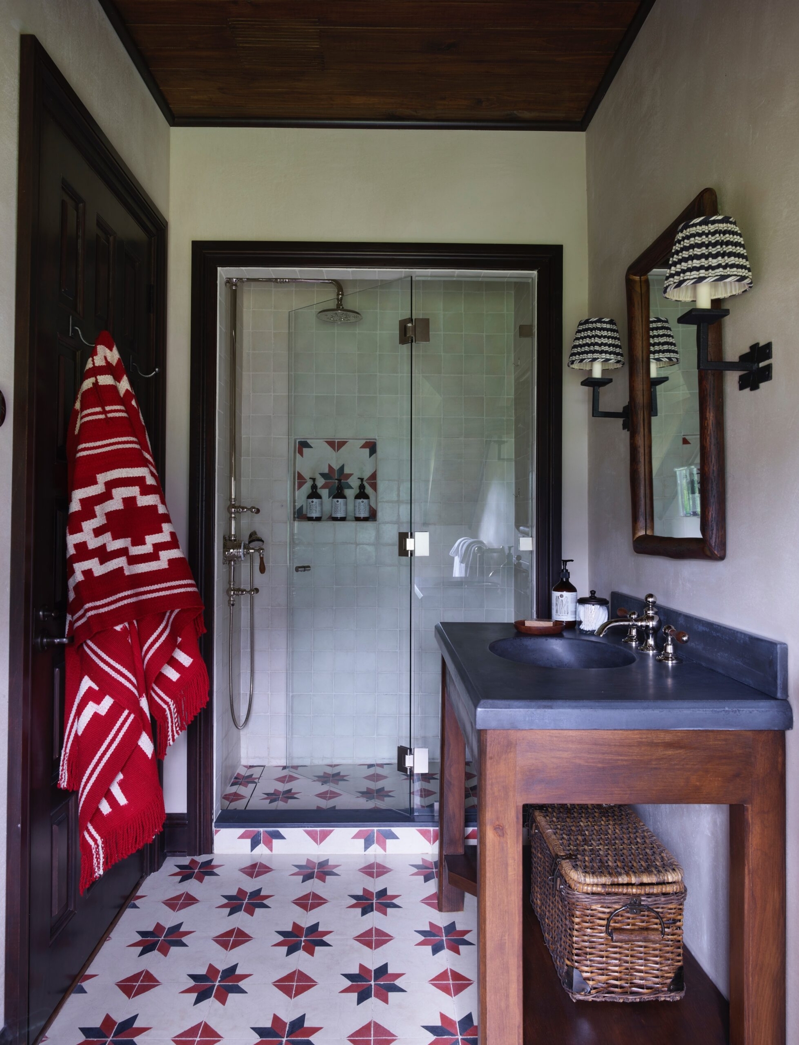 Modern bathroom with star-patterned floor, glass shower, and red towel hanging on door.