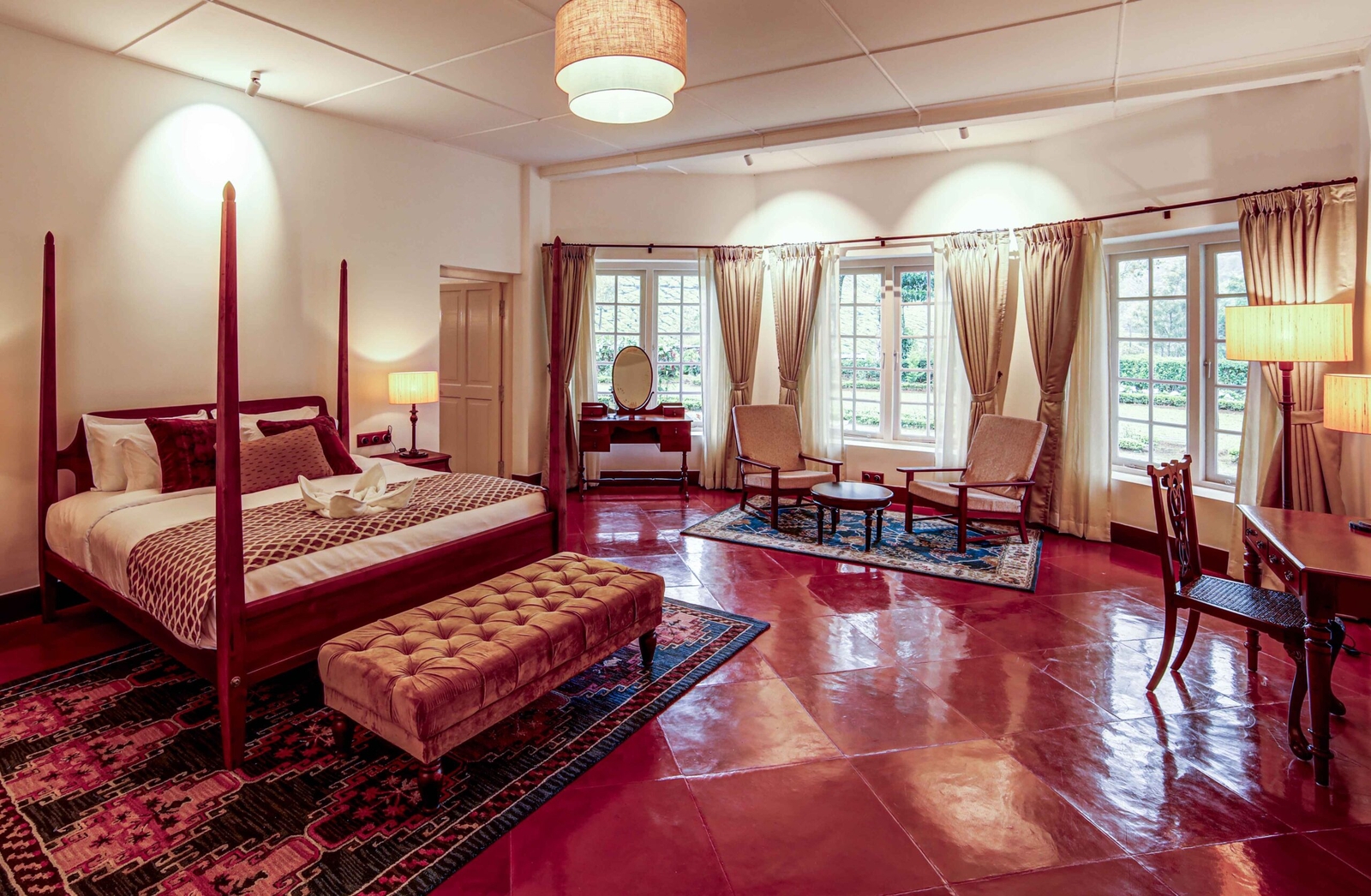 Elegant bedroom with four-poster bed, terracotta floor, and large windows with drapes.