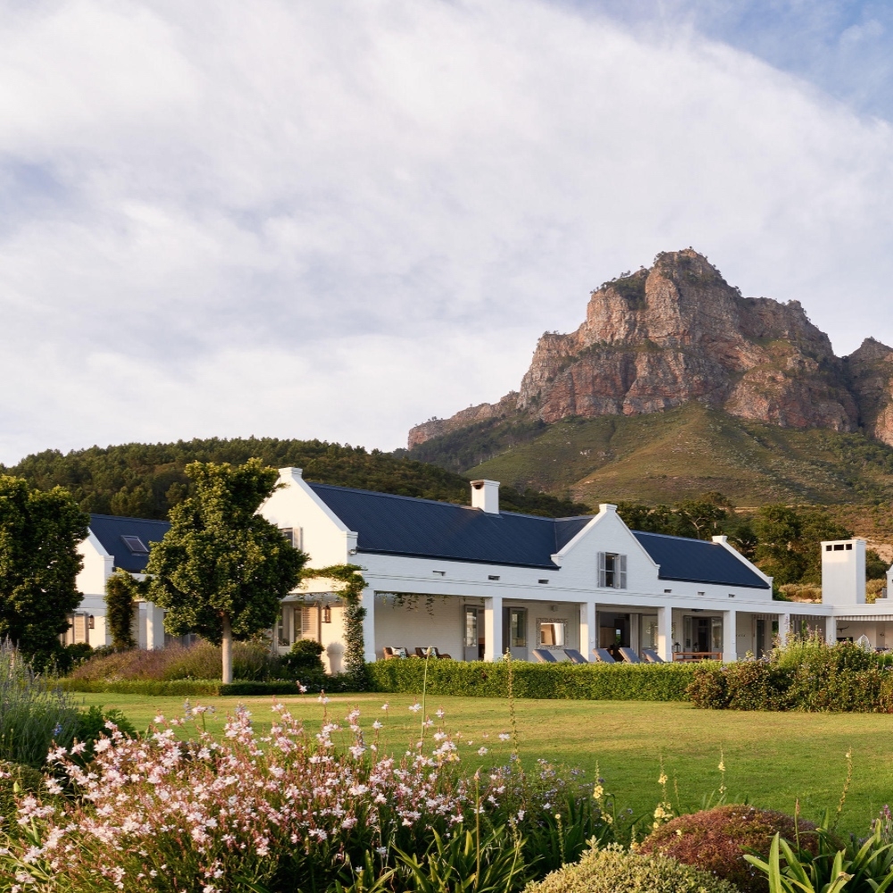 White house with blue roof in front of a mountain and garden.
