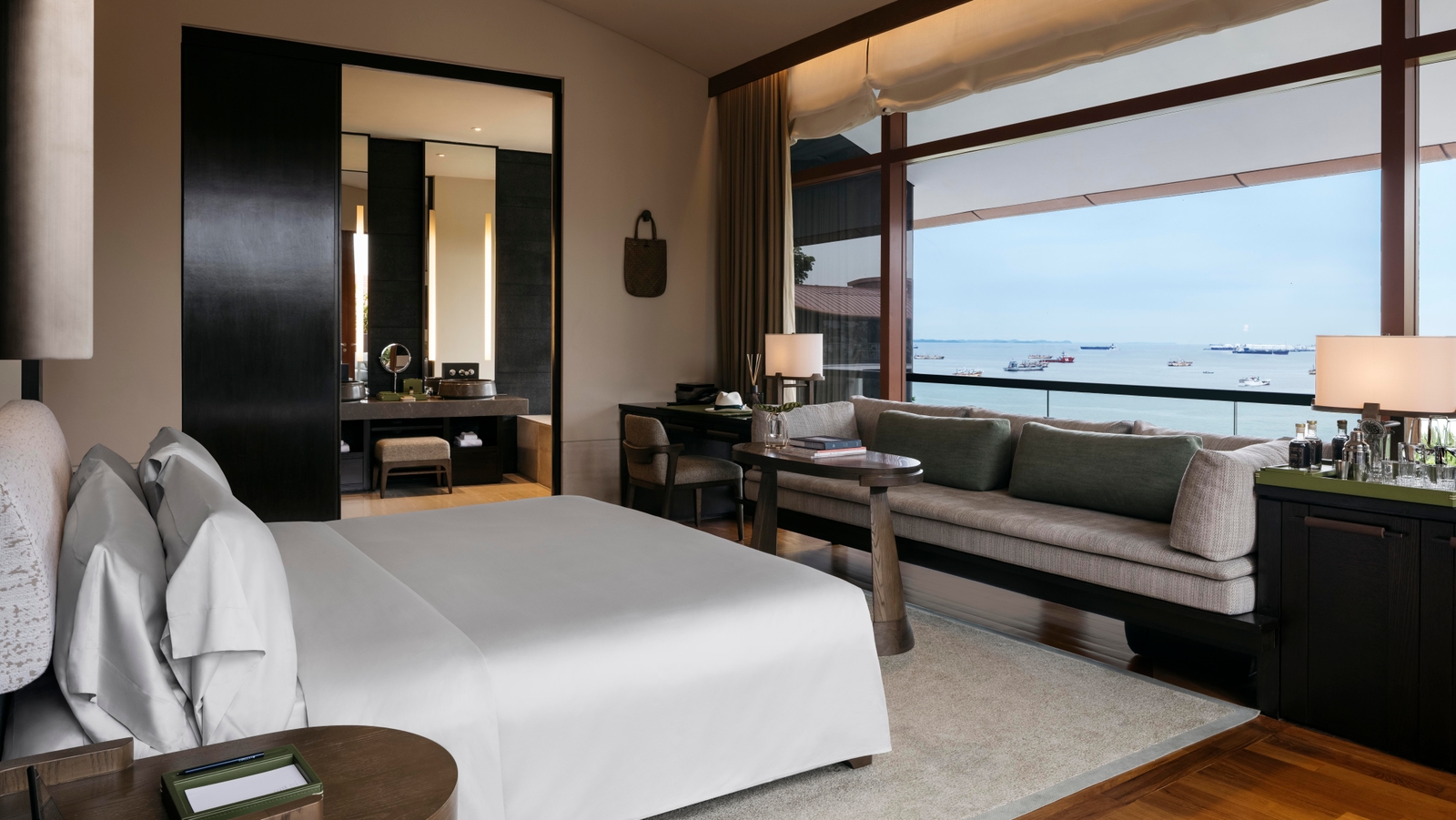 Luxury hotel room with bed, seating area, and large window overlooking the sea with ships.