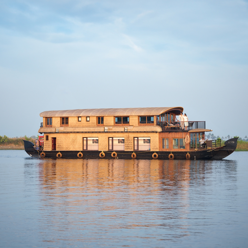 A large, two-story houseboat floating on calm water during sunset.