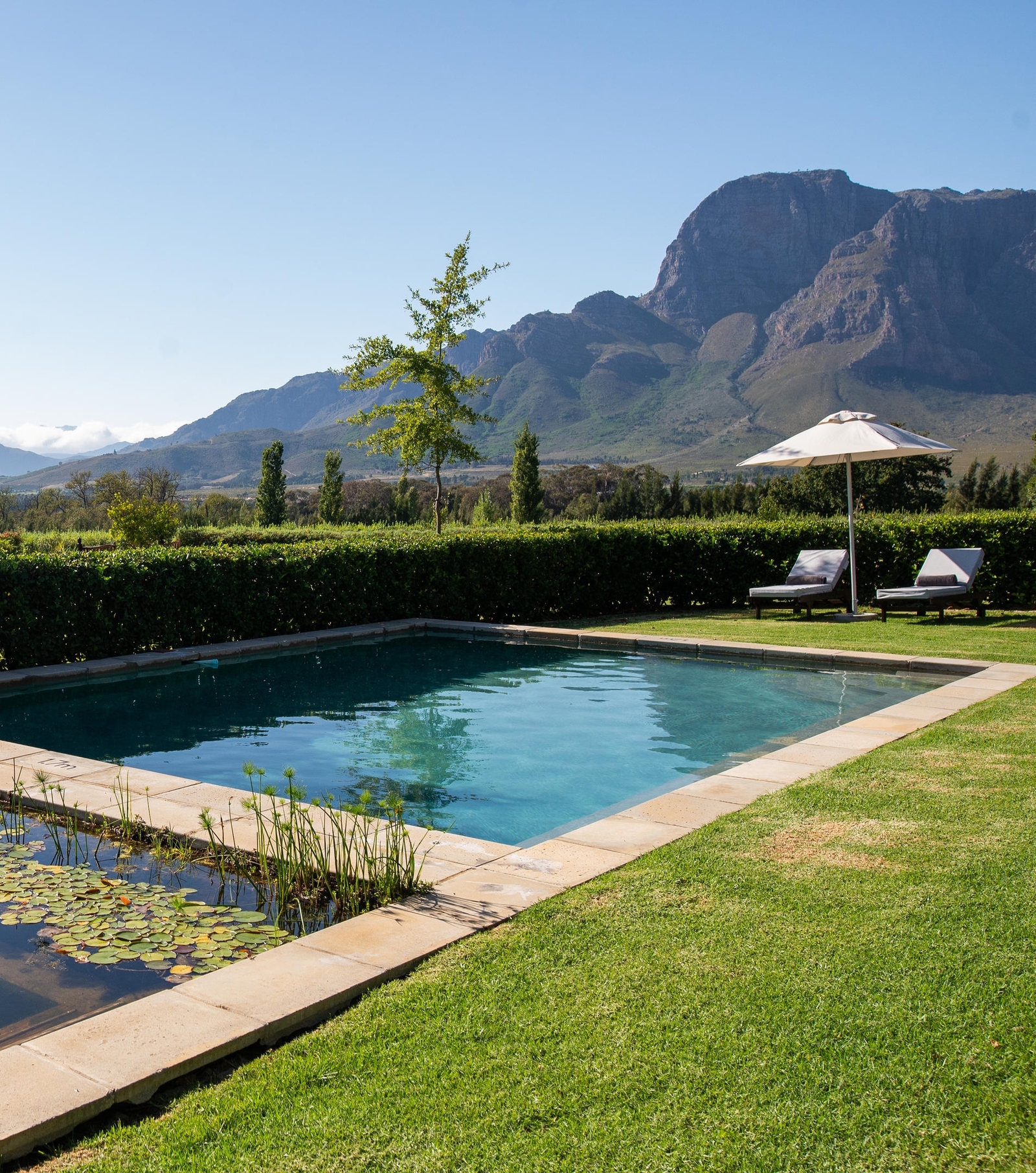 A serene pool with lounge chairs against mountain backdrop under clear blue sky.