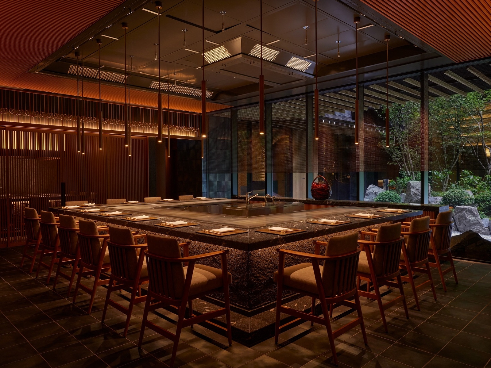 Modern restaurant interior with a teppanyaki grill, wooden chairs, and a view of a zen garden.