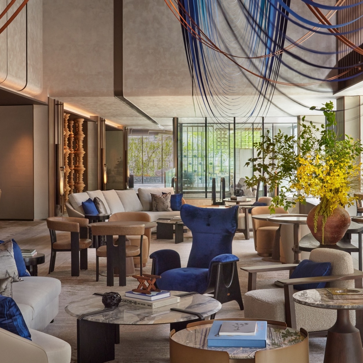 Modern living room with elegant furniture, decorative sculptures, and hanging blue artwork.