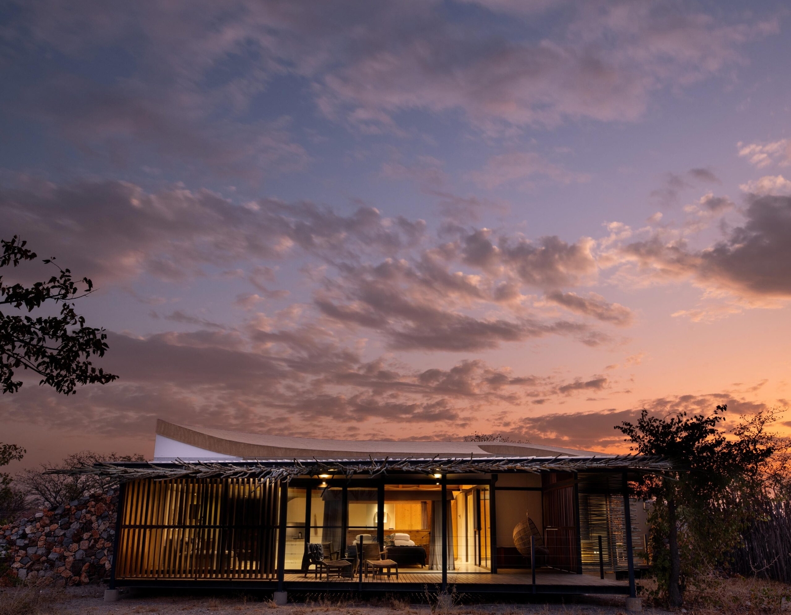 Modern house with large windows at dusk, under a vibrant purple and orange sky.