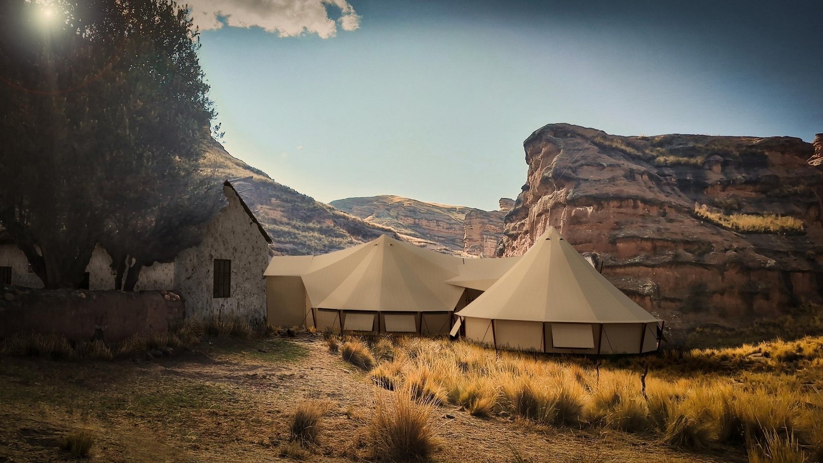 Luxury canvas tents in a field with a backdrop of cliffs and a clear sky.