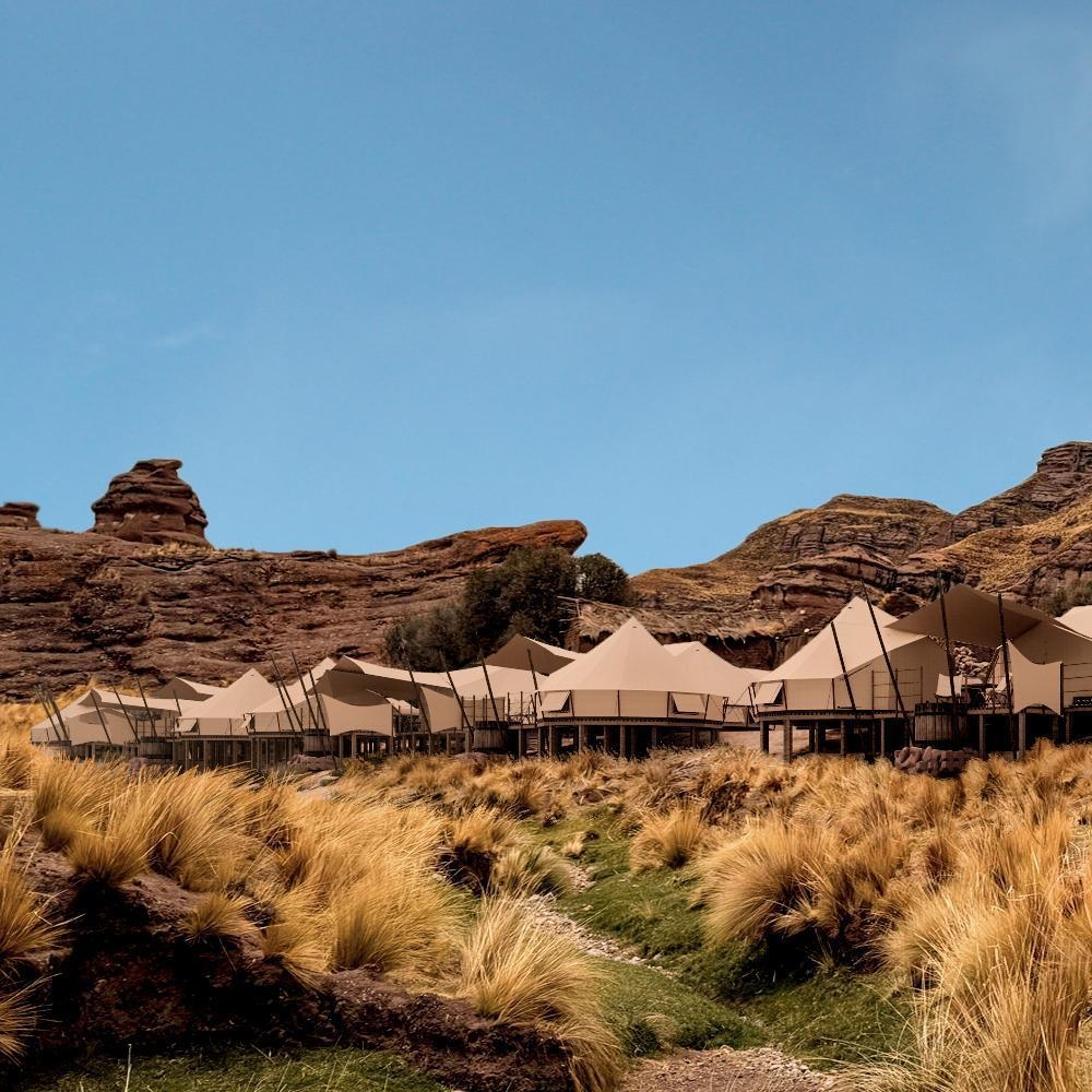 Luxury tents at a desert campsite with rocky terrain in the background.