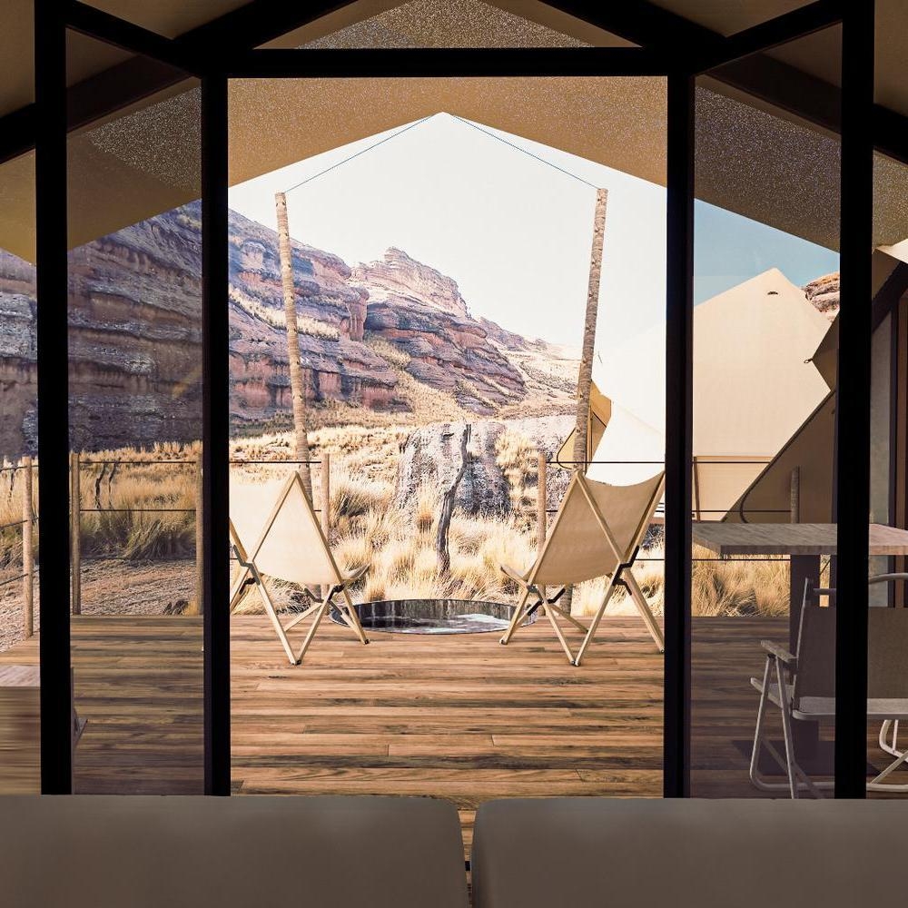 View of a mountainous landscape through the large window of a modern room with two chairs on the porch.