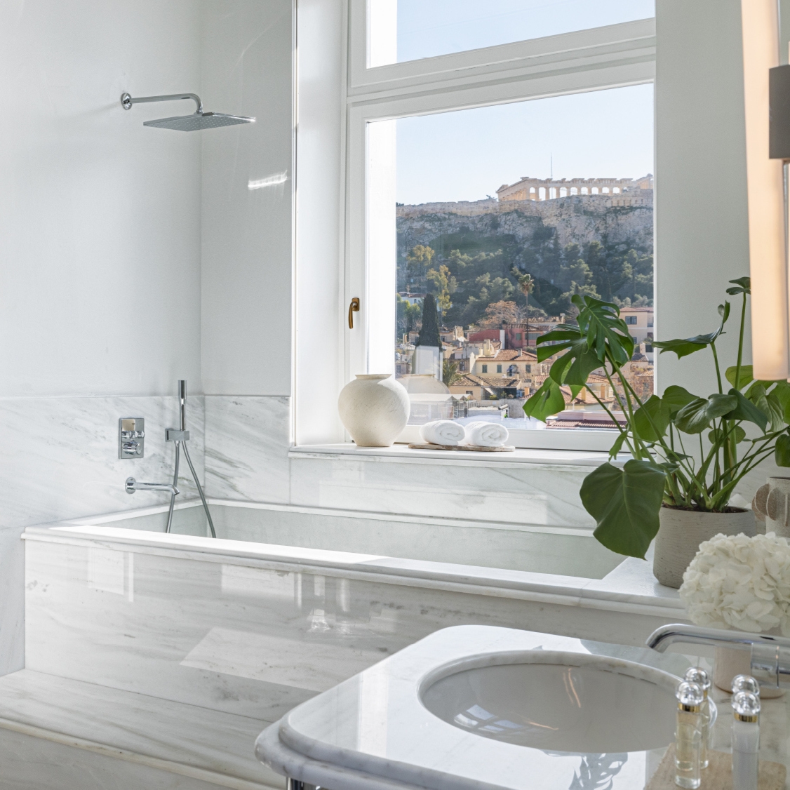 Stylish bathroom featuring a marble bathtub, a round sink, and a view of the Acropolis through large windows.