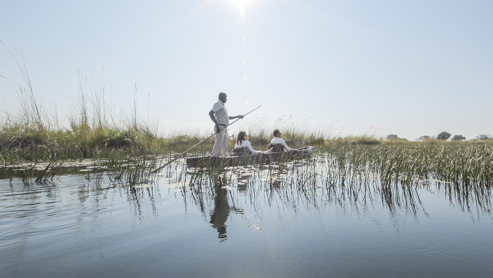 A couple gliding along a waterway on a traditional dugout canoe called a mokoro.