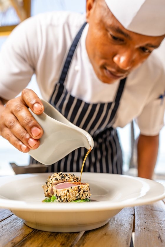 A chef on Alphonse Island pouring sauce onto a dish.