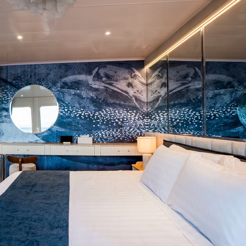 A luxury cabin bedroom featuring a white bed with a blue throw blanket and a large blue sea-inspired mural.
