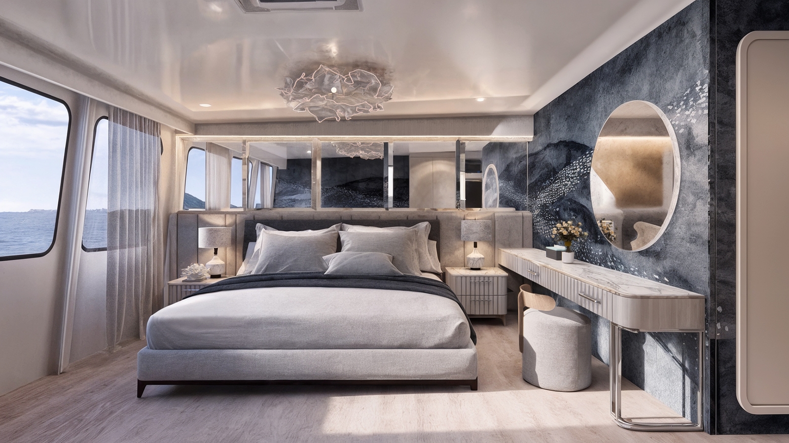 A bedroom with windows looking out to sea. Inside is a double bed with grey sheets and pillows, a crystal chandelier, white carpeting and a vanity mirror along a dark grey wall.