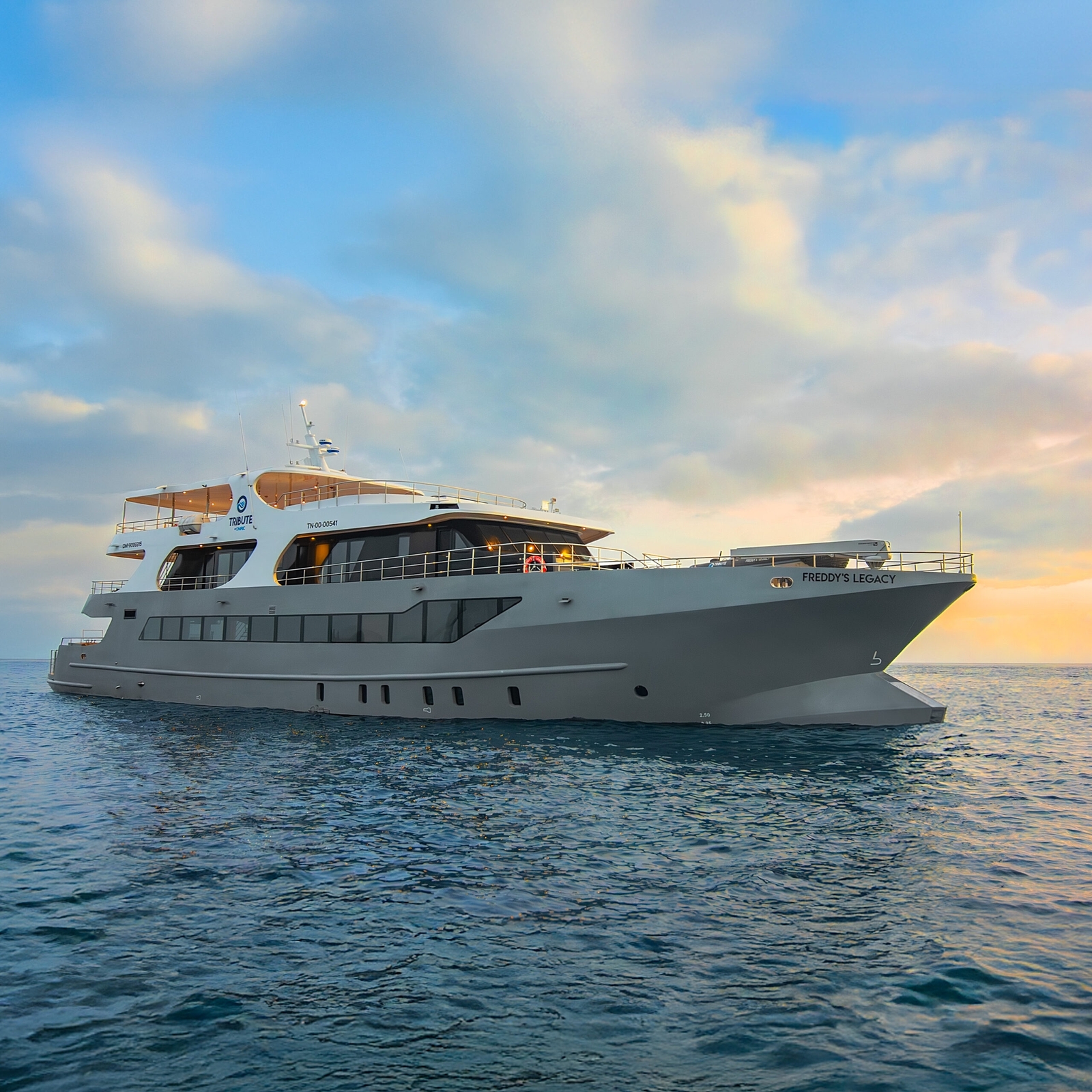 Yacht on blue-grey water with a sunset and cloudy sky in background.