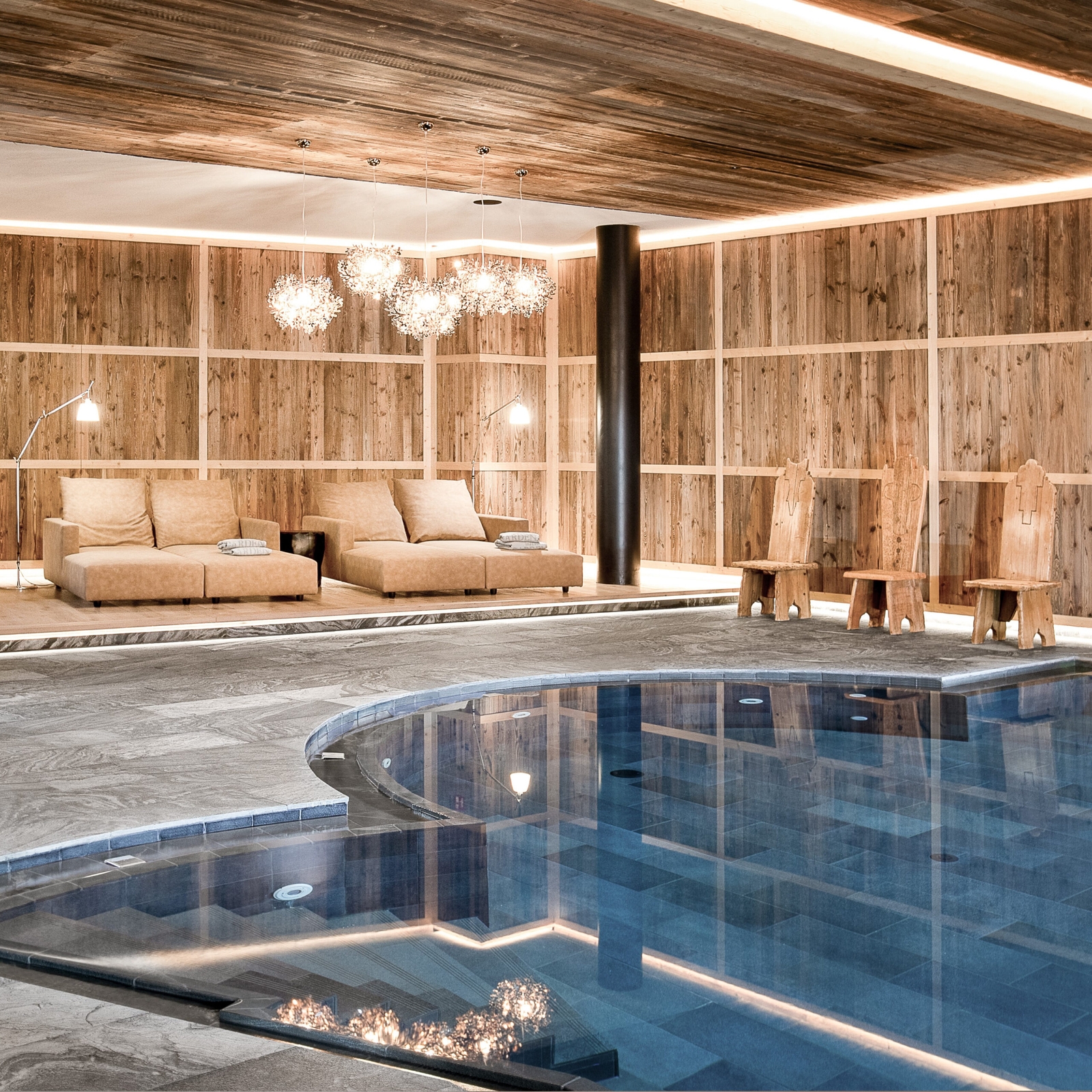 Indoor pool with light blue water and wood walls and ceilings, with tan lounge chairs in the background.