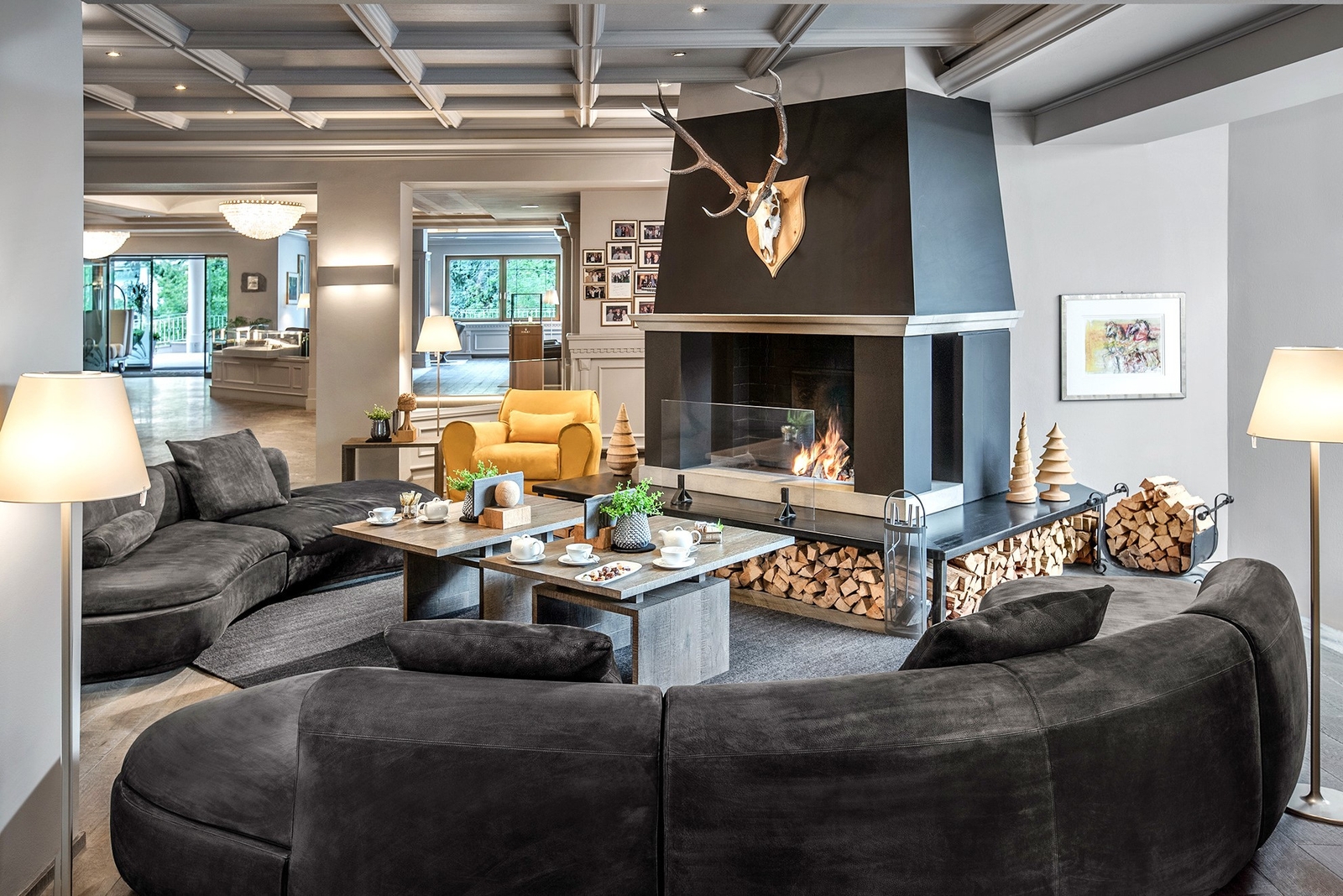 Lounge area with a big wood fireplace painted dark grey around which are a selection of grey plush sofas and a coffee table.