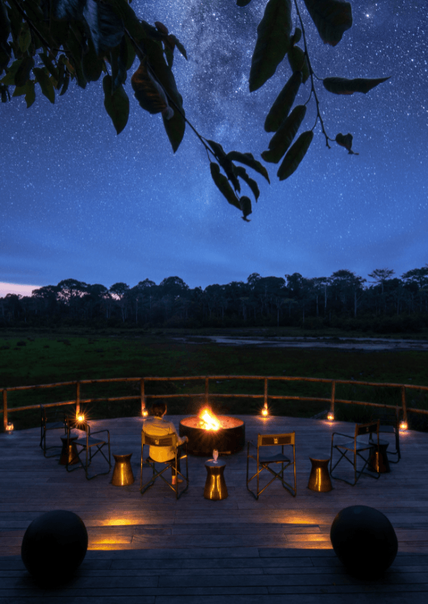 A wooden viewing platform with chairs and a bonfire overlooking the Lango baï at night, with a starry sky above