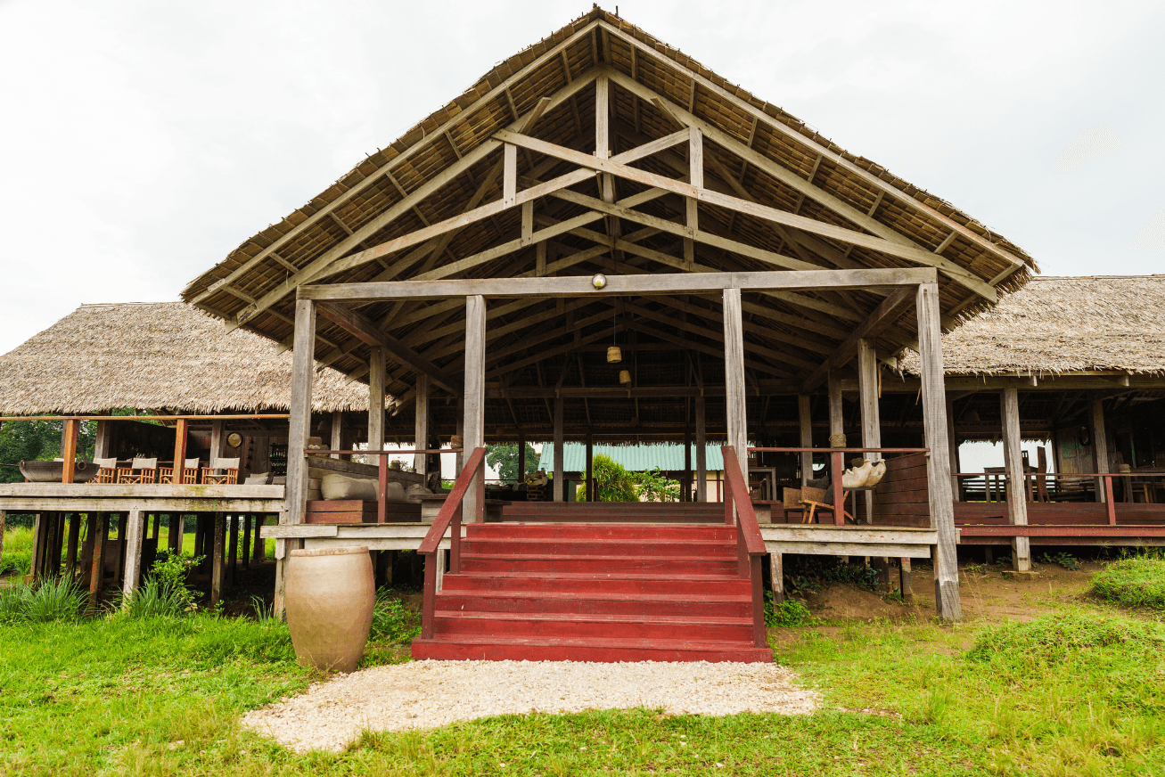 Red stairs leading up to a large raised wooden pavilion with a thatched roof