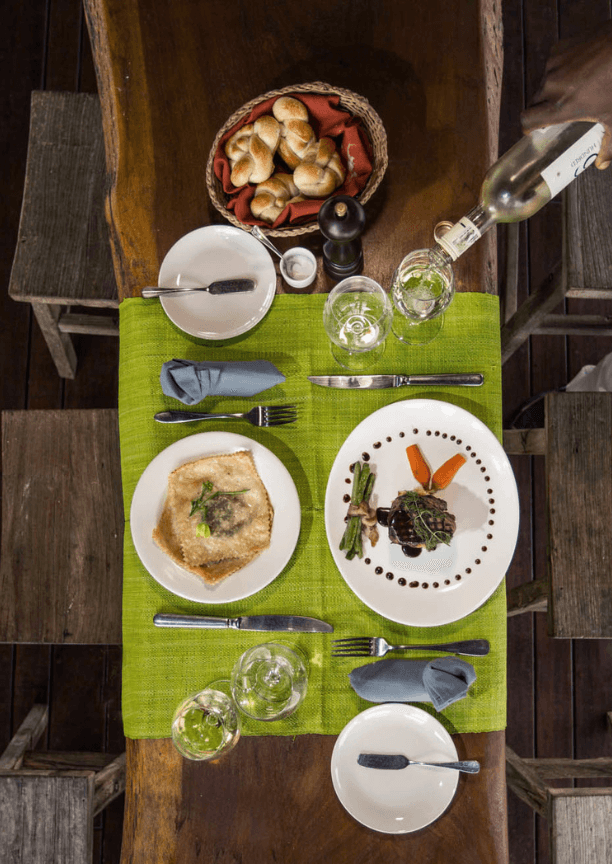 Overhead view of a table covered with a green cloth, wine glasses, two plates of food and a bread basket