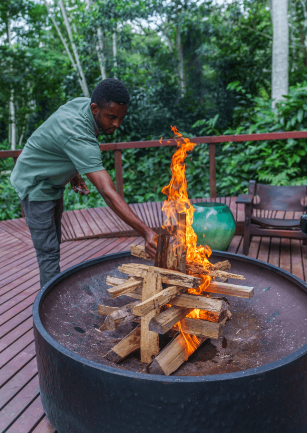 A man tending to a small bonfire in a round pit with stacked wooden logs