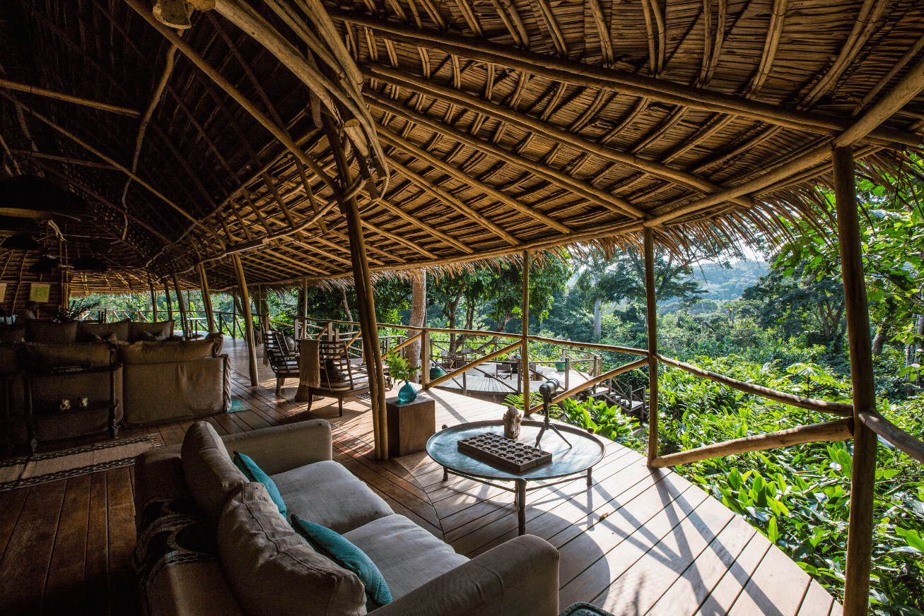 Sitting area on a covered deck with couches, chairs and views of the forest