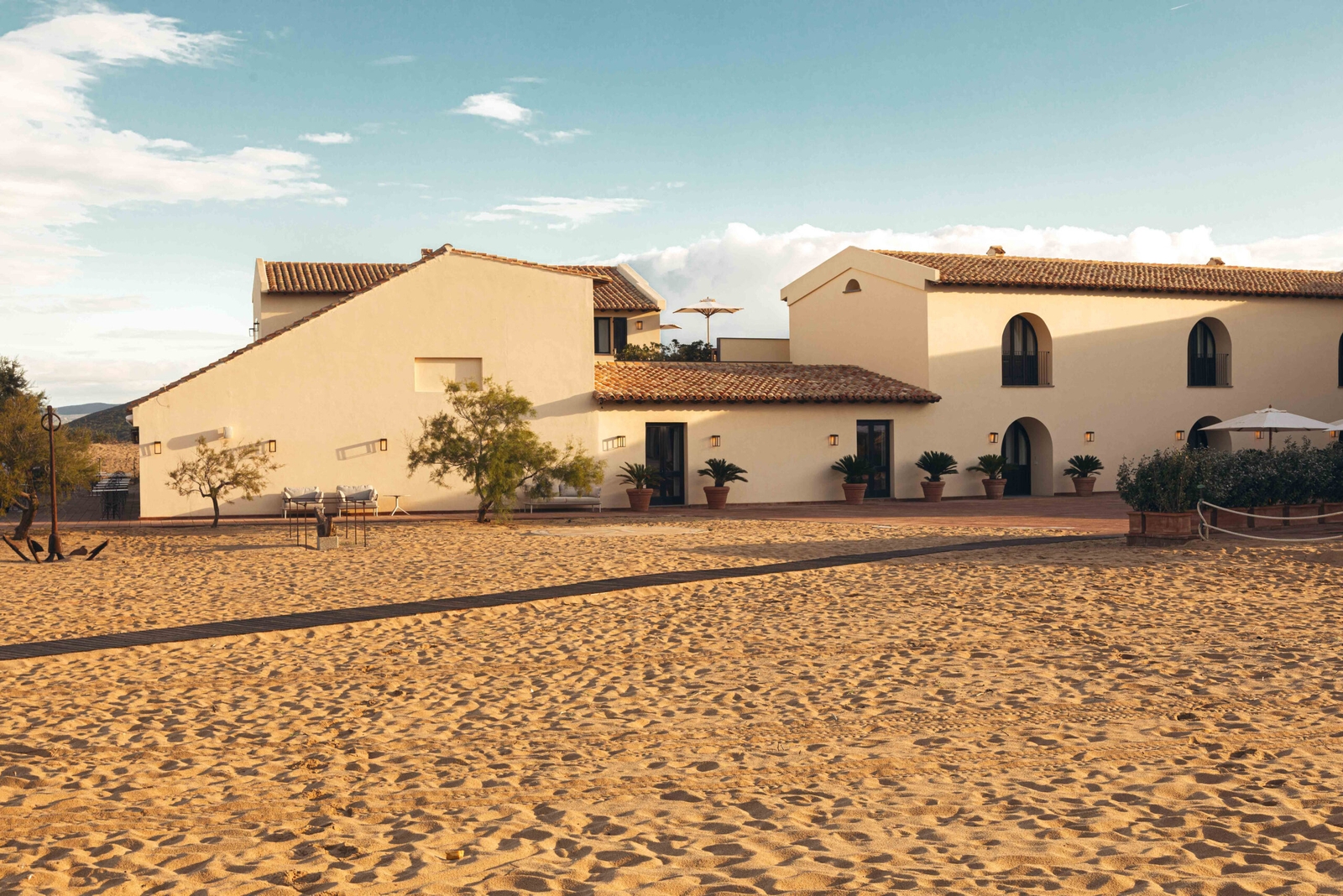 Exterior view of the villa with white walls and red-tile roofs, and a wide stretch of sand in the foreground.