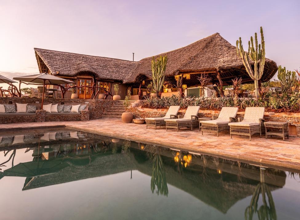 Private Wilderness lodge with a large thatched roof, poolside lounge chairs, and desert plants reflected in the water.