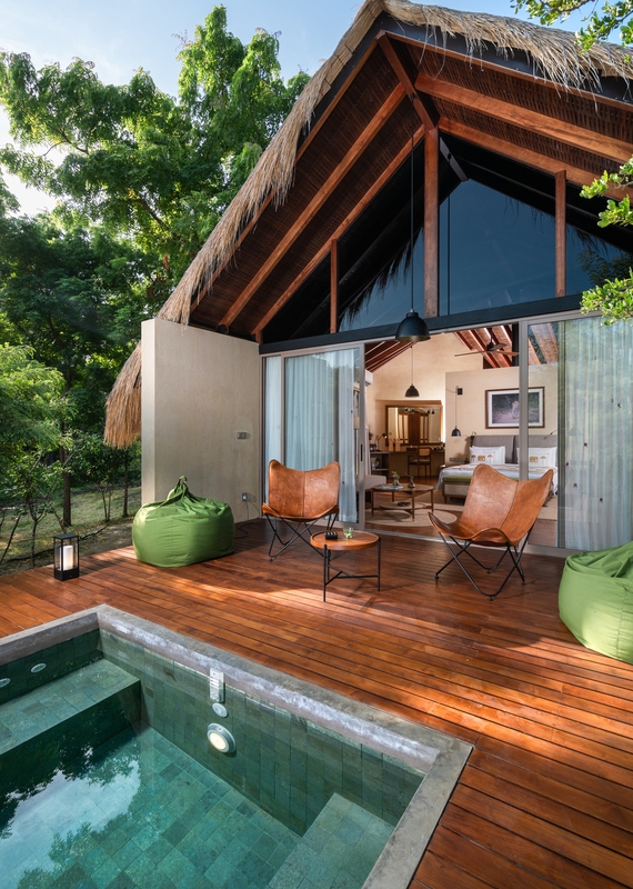 A luxurious villa with a thatched roof, a private stone plunge pool, and leather chairs on a sunlit deck.