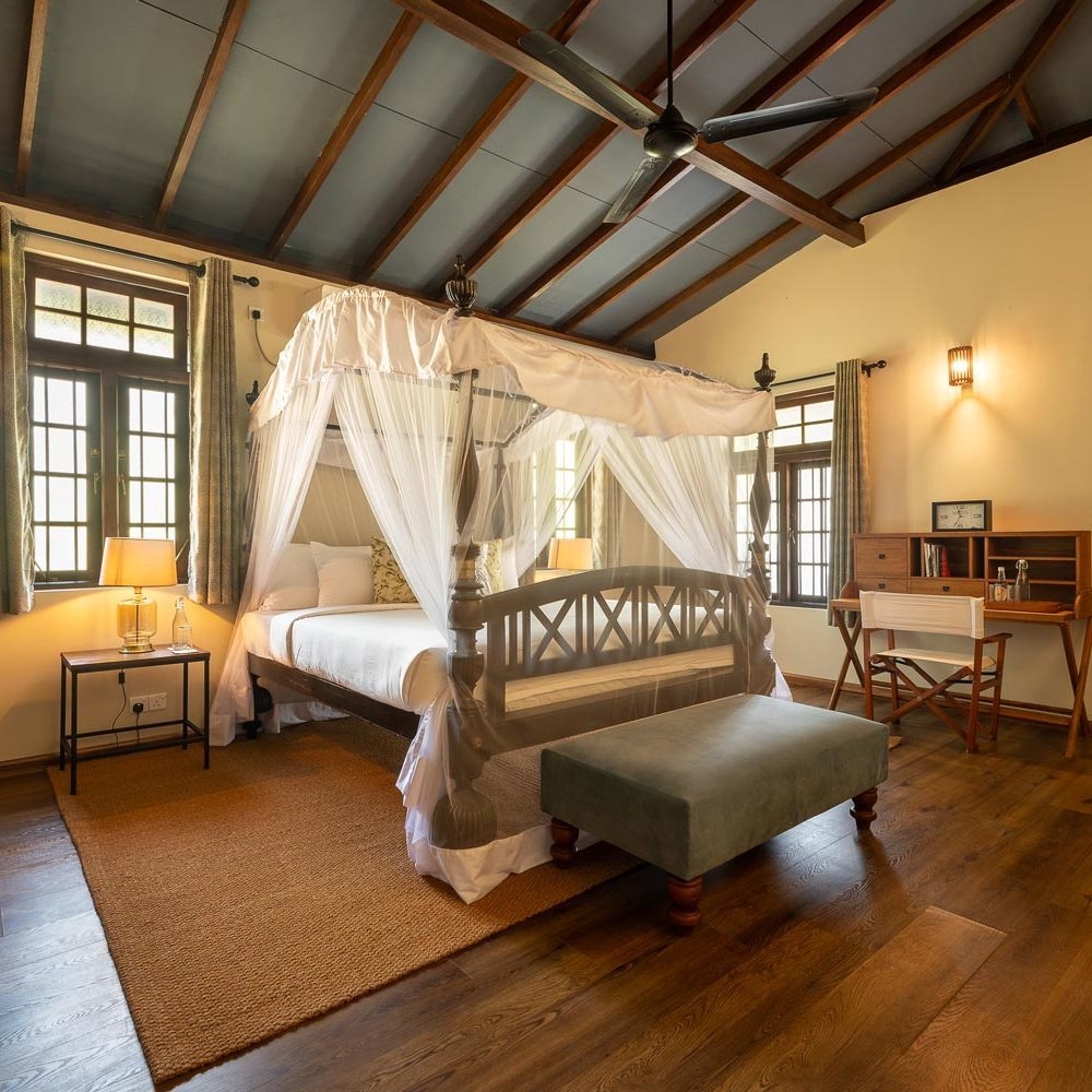 Elegant bedroom with a white canopy bed, wooden desk, and large windows under a beamed ceiling.