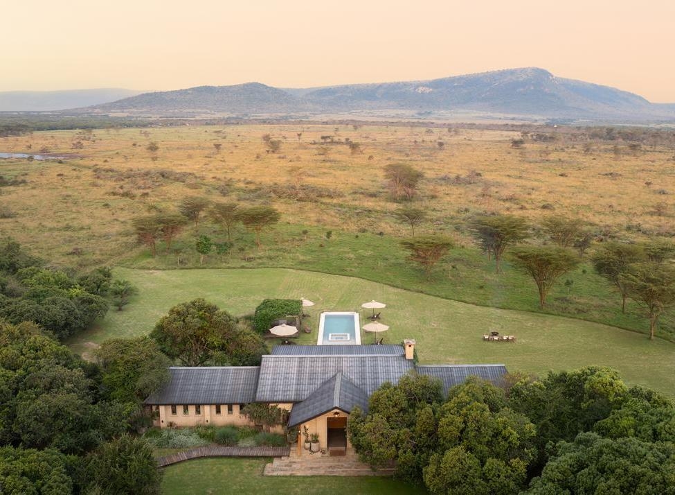 High-angle view of Amani House surrounded by trees overlooking a wide, grassy plain and distant mountains.